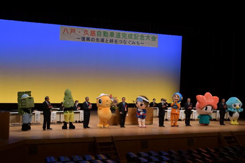 八戸久慈自動車道記念大会　壇上に並ぶ沿岸6市町村長とそのマスコットたち
